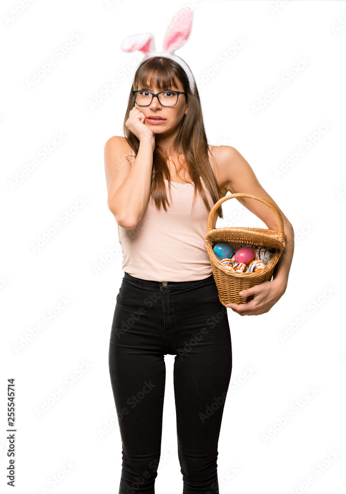 Young woman wearing bunny ears for Easter holidays is a little bit nervous and scared putting hands to mouth on isolated white background Young woman wearing bunny ears for Easter holidays is a little bit nervous and scared putting hands to mouth on isolated white background