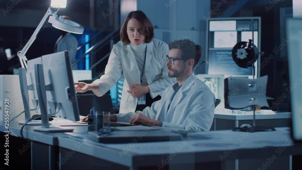Machine Engine Development Engineer Working on Computer at His Desk, Talks with Female Project Manager. Team of Professionals Working in the Modern Industrial Design Laboratory