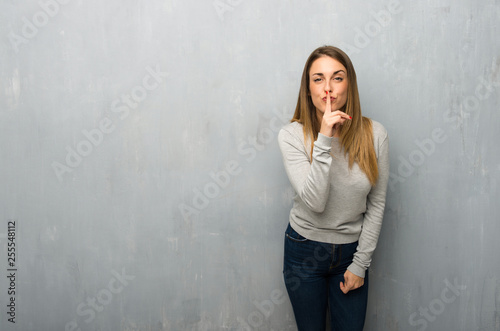 Young woman on textured wall showing a sign of silence gesture putting finger in mouth