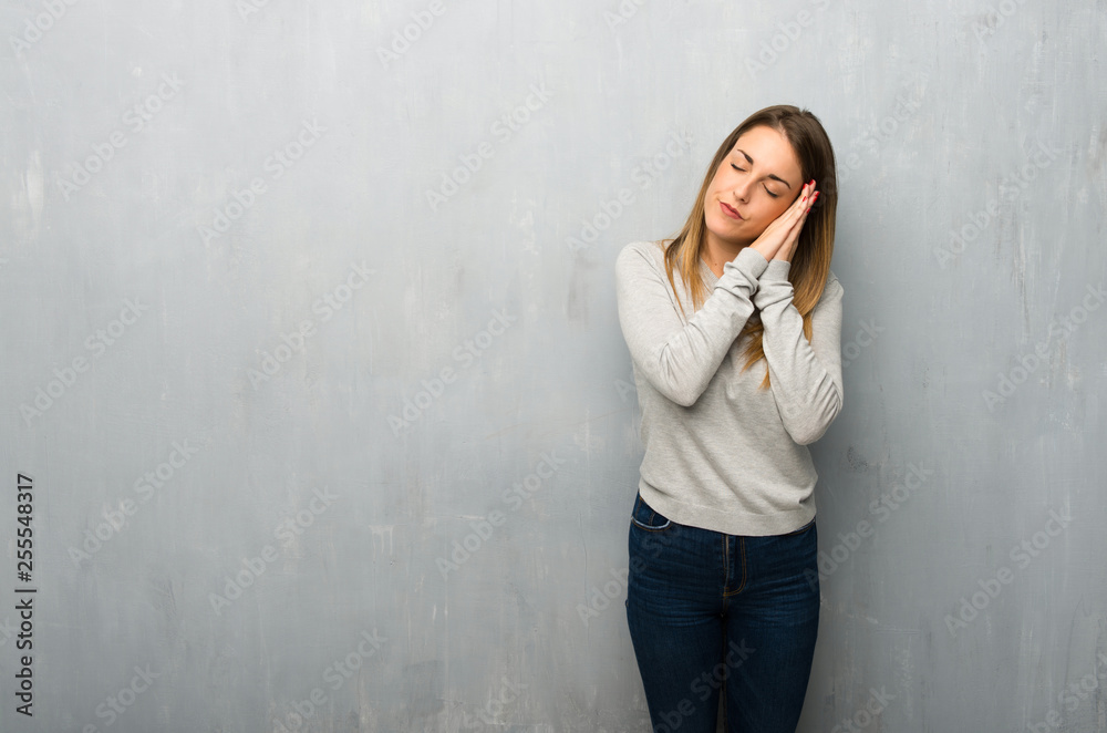 Young woman on textured wall making sleep gesture in dorable expression Young woman on textured wall making sleep gesture in dorable expression