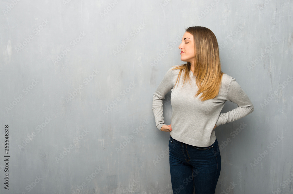 Young woman on textured wall suffering from backache for having made an effort