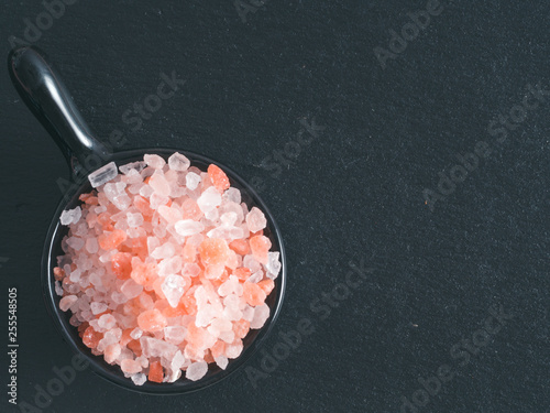 Himalayan pink salt in small black bowl on black stone background. Copy space