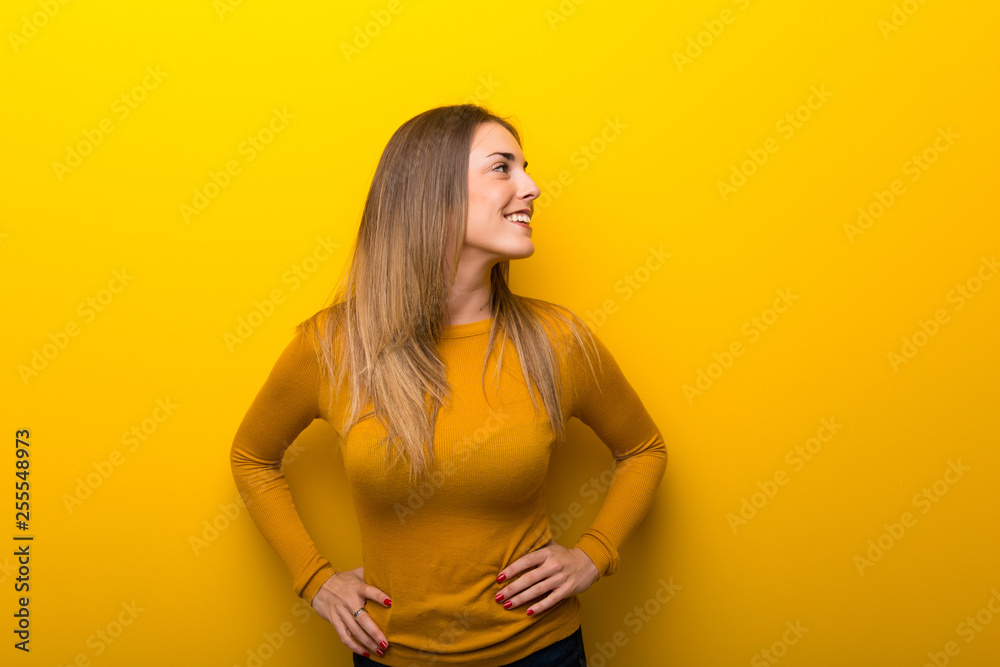 Obraz premium Young woman on yellow background posing with arms at hip and laughing