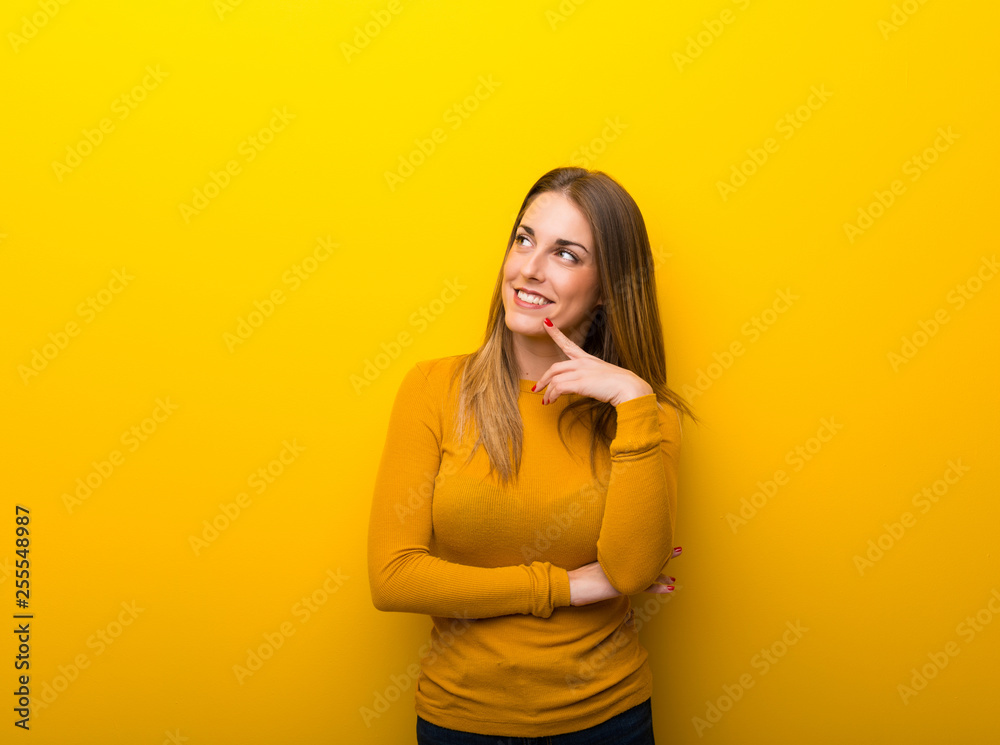 Young woman on yellow background thinking an idea while looking up Young woman on yellow background thinking an idea while looking up