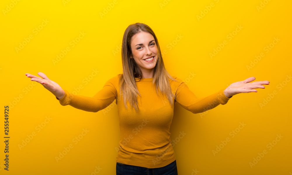 Young woman on yellow background presenting and inviting to come with hand