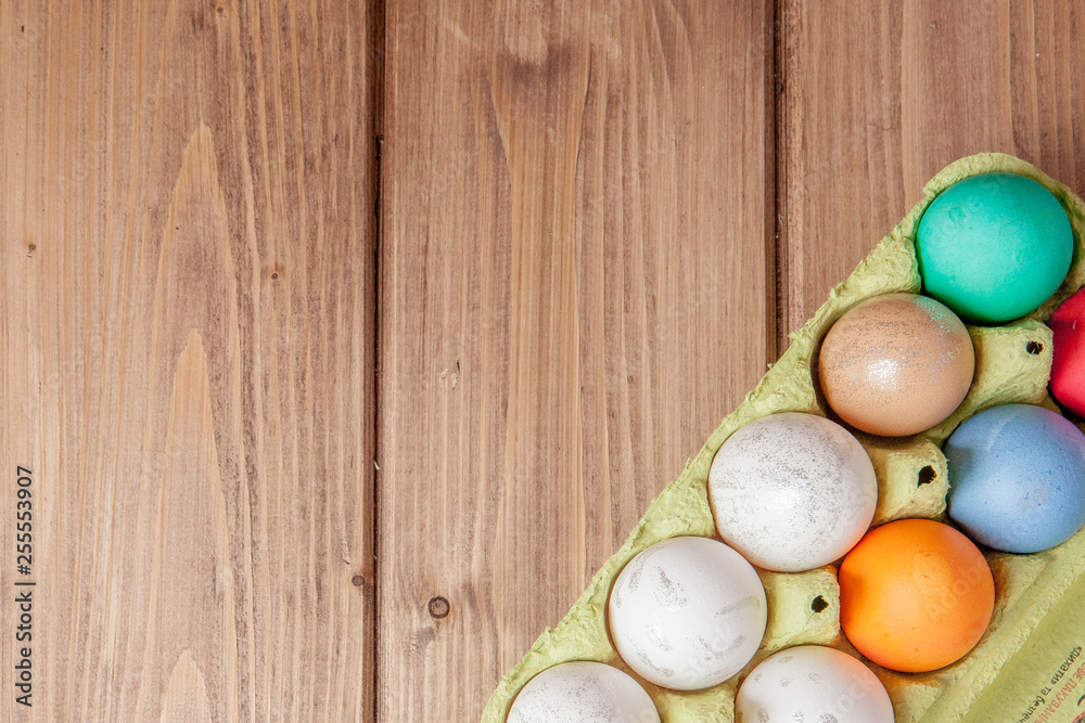 Colorful Easter eggs in box on wooden background with copy space