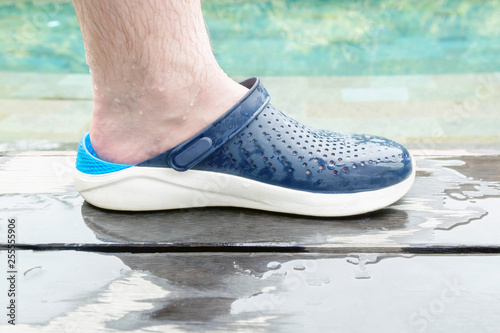 Wet male hairy leg in comfortable rubber summer shoes by the private pool.