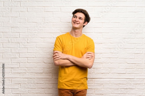 Teenager man over white brick wall looking up while smiling