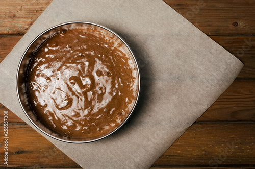 Fotografia Cake pan with chocolate batter and wooden spoon close up on dark wooden background