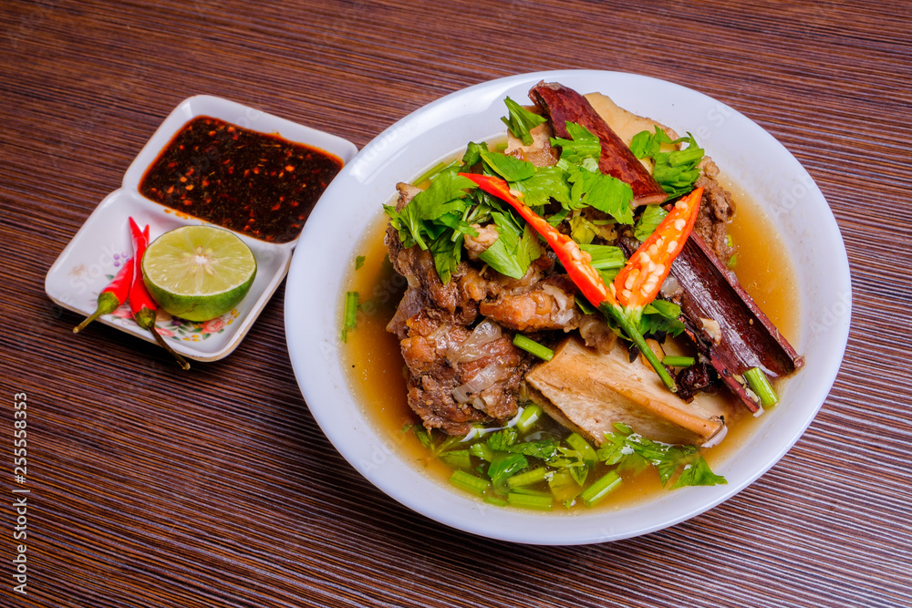 Cow bone soup or Sup Tulang in Malay with chilli and soya sauce . Muslim food in white bowl on dark brown wooden plate . Selective focus . Cow bone soup or Sup Tulang in Malay with chilli and soya sauce . Muslim food in white bowl on dark brown wooden plate . Selective focus .