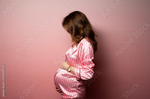 Beautiful brunette pregnant model in pink suit on pink background