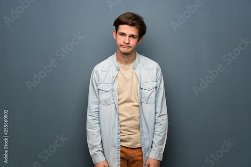 Teenager man with jean jacket over grey wall with sad and depressed expression