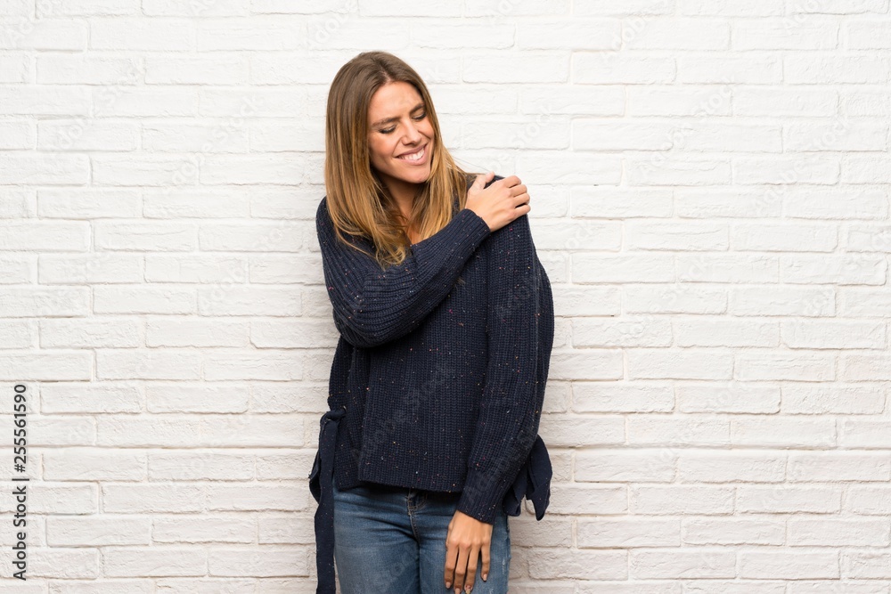 Blonde woman over brick wall suffering from pain in shoulder for having made an effort