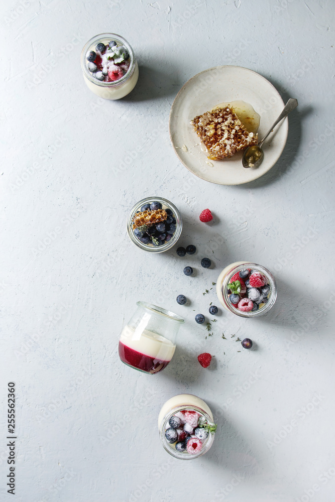 Homemade classic dessert Panna cotta with raspberry and blueberry berries and jelly in jars, decorated by mint, sugar powder, honey combs over grey texture background. Flat lay, space Homemade classic dessert Panna cotta with raspberry and blueberry berries and jelly in jars, decorated by mint, sugar powder, honey combs over grey texture background. Flat lay, space