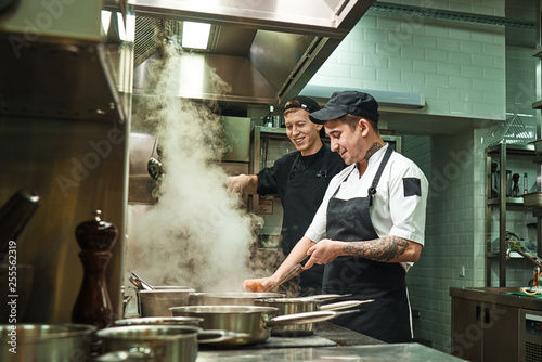 Positive mood. Side view of two cheerful and smiling cooks in uniform are preparing a food in a kitchen restaurant photo