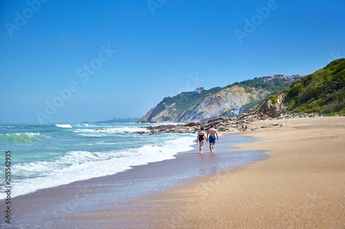 Fototapeta Naklejka Na Ścianę i Meble -  Elderly couple walking along a sandy beach. Holidays on the coast of the Atlantic Ocean in southwestern France