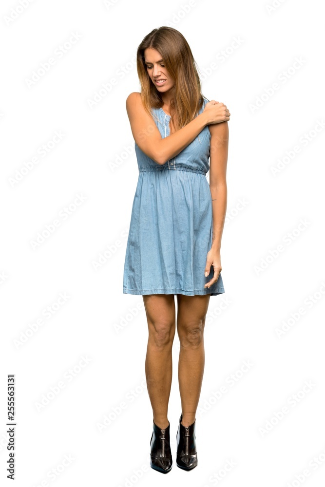A full-length shot of a Blonde woman with jean dress suffering from pain in shoulder for having made an effort over isolated white background A full-length shot of a Blonde woman with jean dress suffering from pain in shoulder for having made an effort over isolated white background