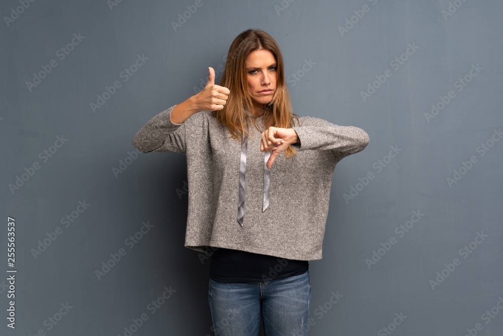 Blonde woman over grey background making good-bad sign. Undecided ...