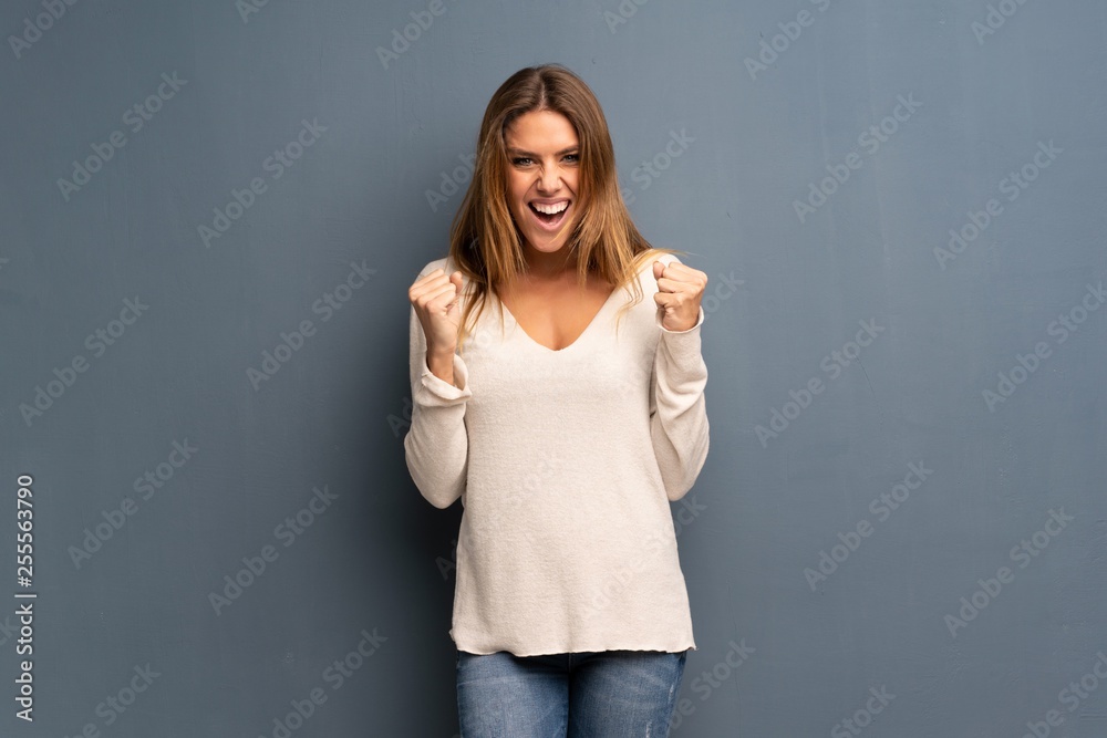 Blonde woman over grey background celebrating a victory in winner position Blonde woman over grey background celebrating a victory in winner position
