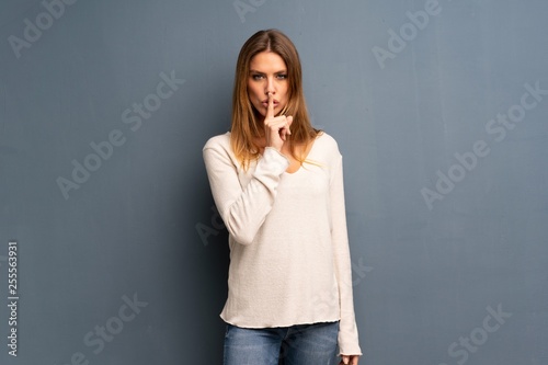Blonde woman over grey background showing a sign of silence gesture putting finger in mouth