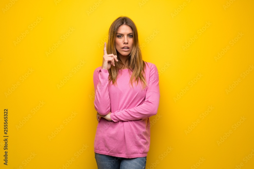 Woman with pink sweater over yellow wall thinking an idea pointing the finger up Woman with pink sweater over yellow wall thinking an idea pointing the finger up