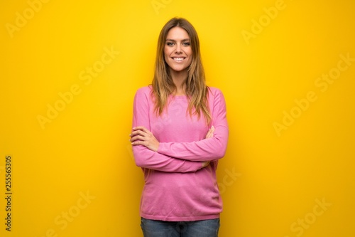 Woman with pink sweater over yellow wall keeping the arms crossed in frontal position