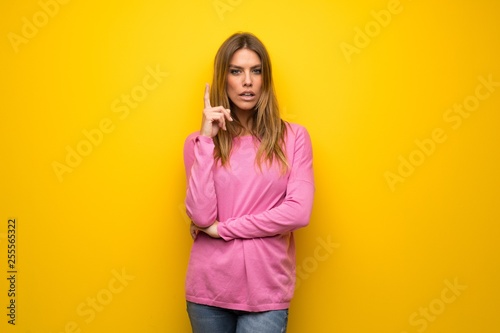 Woman with pink sweater over yellow wall thinking an idea pointing the finger up