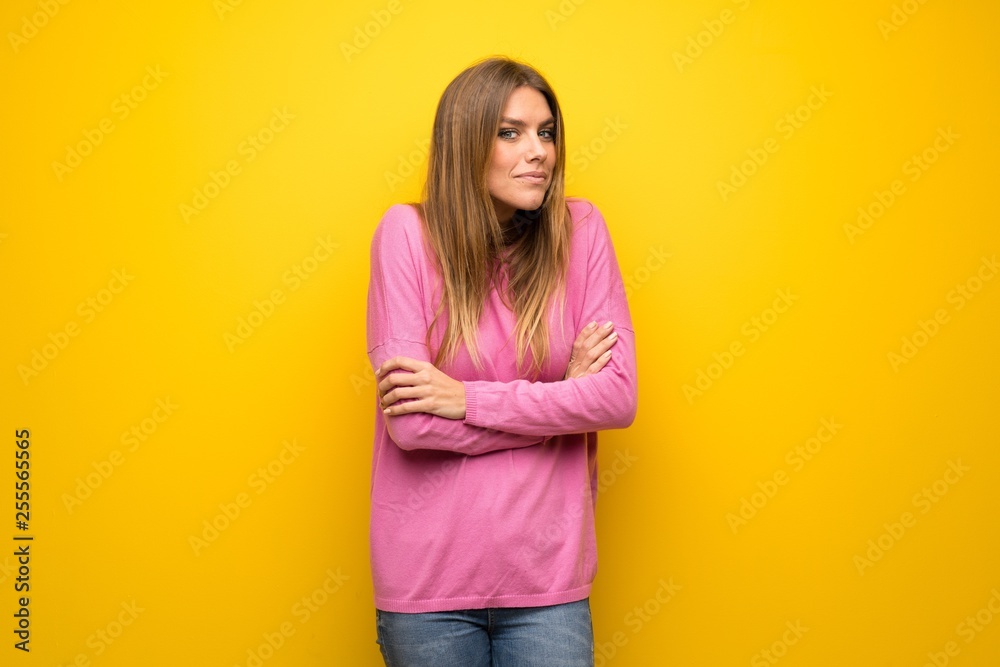 Woman with pink sweater over yellow wall making doubts gesture while lifting the shoulders Woman with pink sweater over yellow wall making doubts gesture while lifting the shoulders