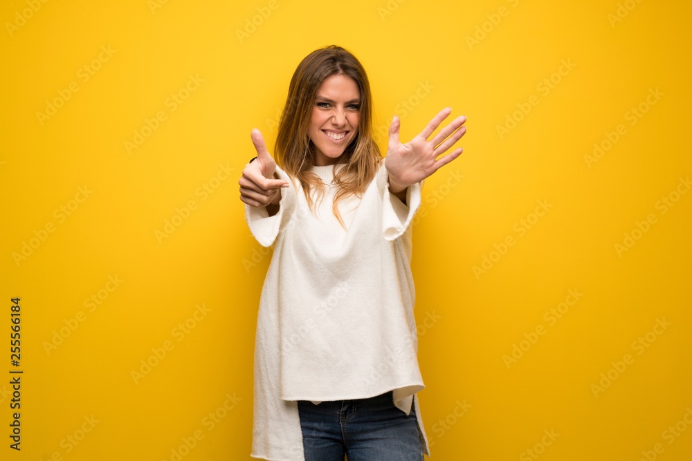 Blonde woman over yellow wall counting six with fingers Blonde woman over yellow wall counting six with fingers
