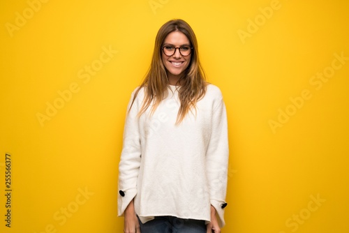 Blonde woman over yellow wall with glasses and happy © luismolinero