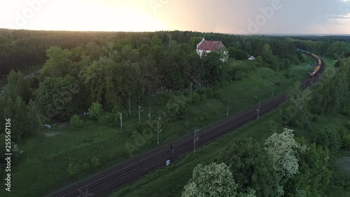 Aerial shot of cargo train running through the Church small village in the woods at sunset