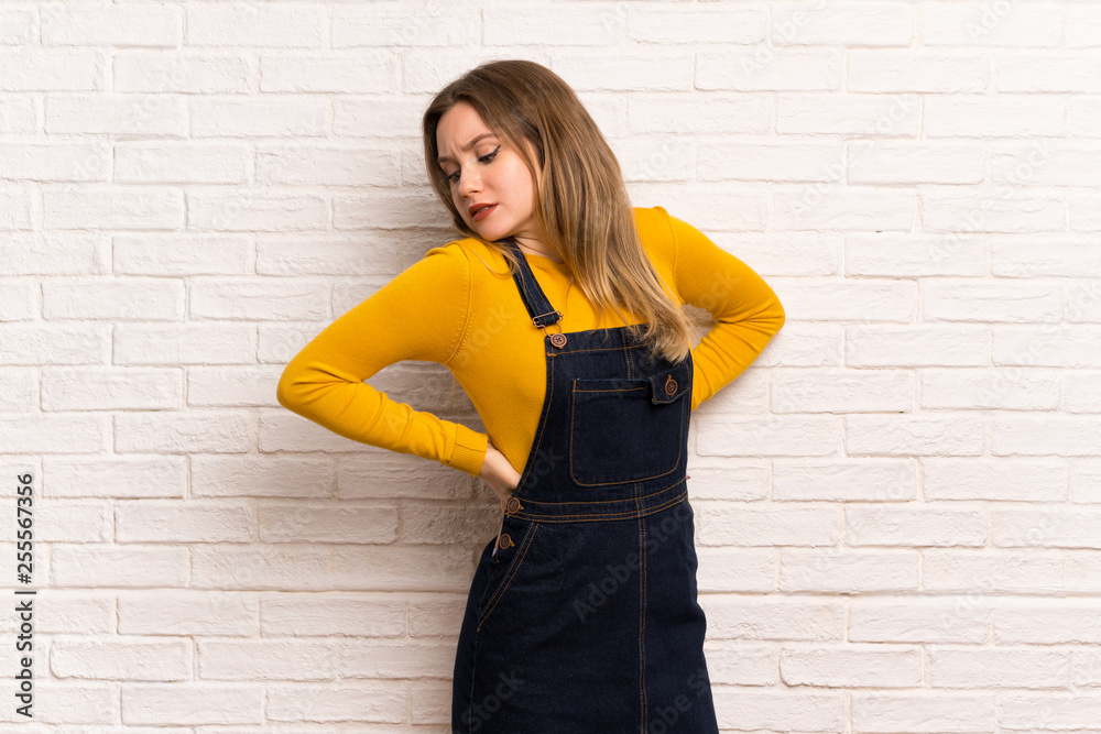 Teenager girl over white brick wall suffering from backache for having made an effort Teenager girl over white brick wall suffering from backache for having made an effort