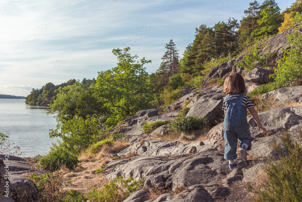 A young girl climbs over the rocks on top of a hill. A little girl climbs a mountain. Overcoming difficulties.
