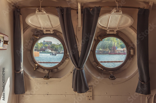 Two portholes with a view of the river and the boat.