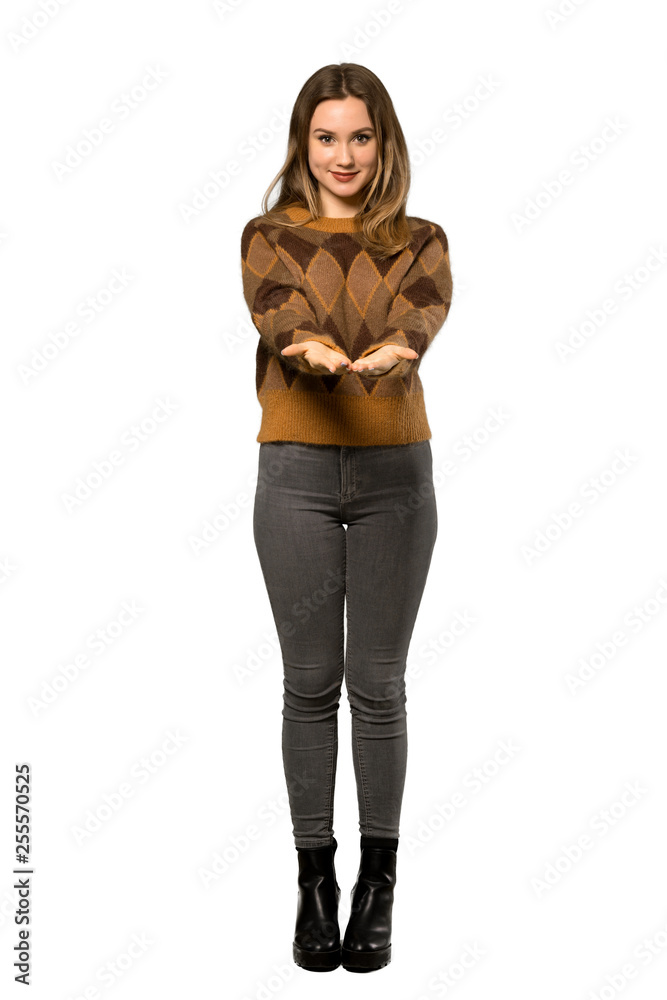 Fototapeta premium A full-length shot of a Teenager girl with brown sweater holding copyspace imaginary on the palm to insert an ad over isolated white background