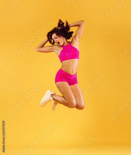 Strong athletic, woman, jumping on yellow background wearing sportswear. Fitness and sport motivation.