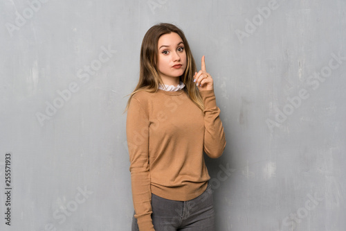 Teenager girl over textured wall thinking an idea pointing the finger up