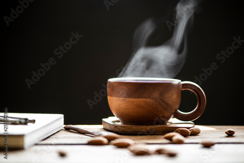 Hot tea with steam in wood cup and almonds on the wooden table black background.