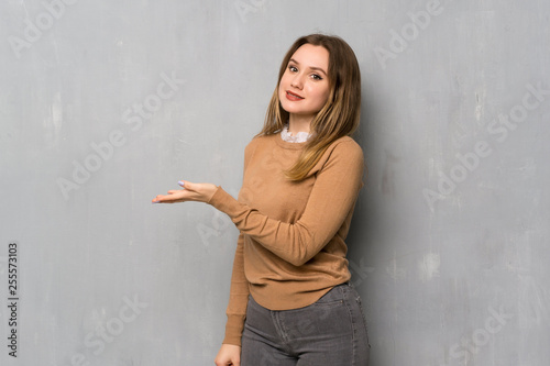 Teenager girl over textured wall presenting an idea while looking smiling towards
