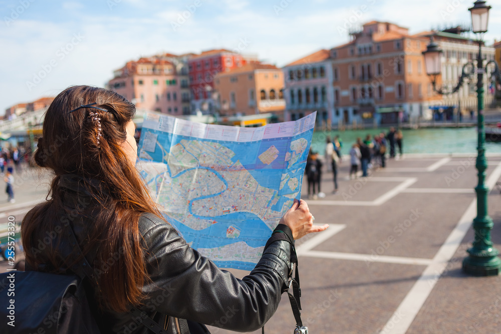 Young woman  looking at paper map of Venice on sunny day, many tourists on background