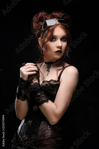 A beautiful redhead cosplayer girl wearing a Victorian-style steampunk costume with big breasts in a deep neckline looks surprised and scared. Portrait. Black background.