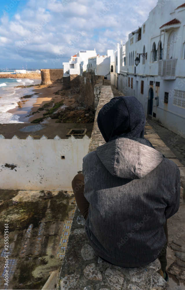 Landmark of Asilah - Atlantic Ocean Surf and Old City Wall with white houses on Seaside. Man sitting on the Wall of Asilah, Morocco