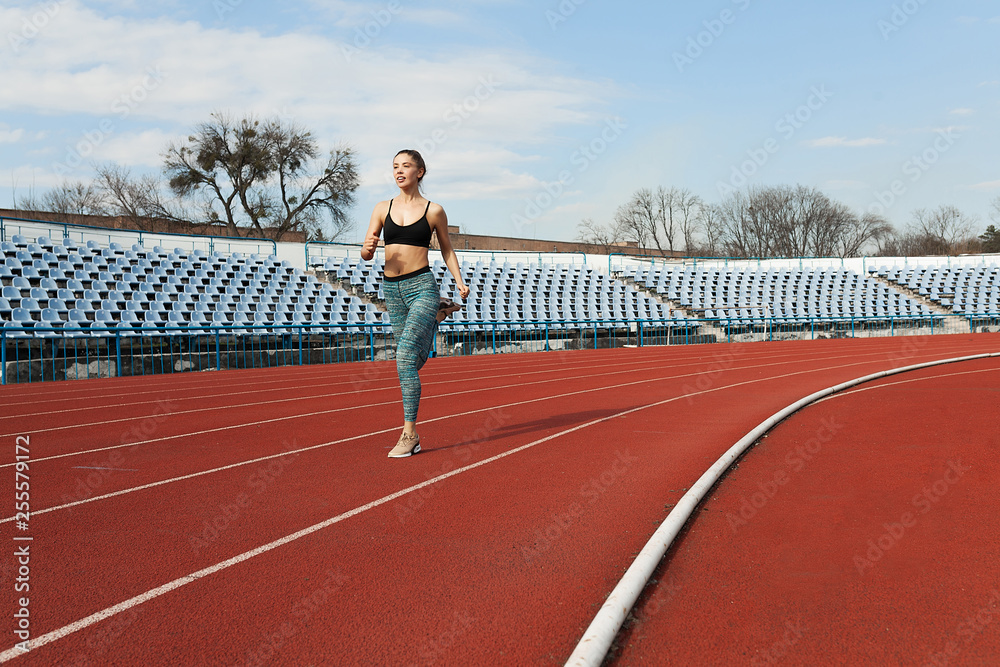 Obraz premium Young woman running during sunny morning on stadium track
