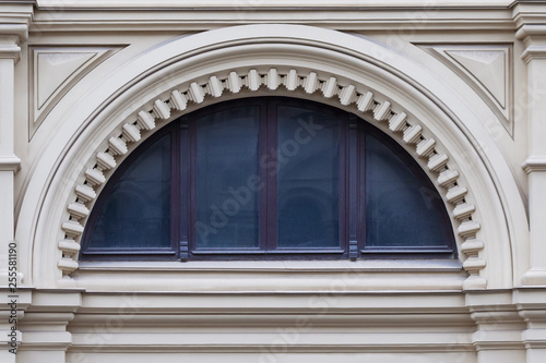 Close up view on a  semicircular window on a facade of white stone ancient building with carved decor