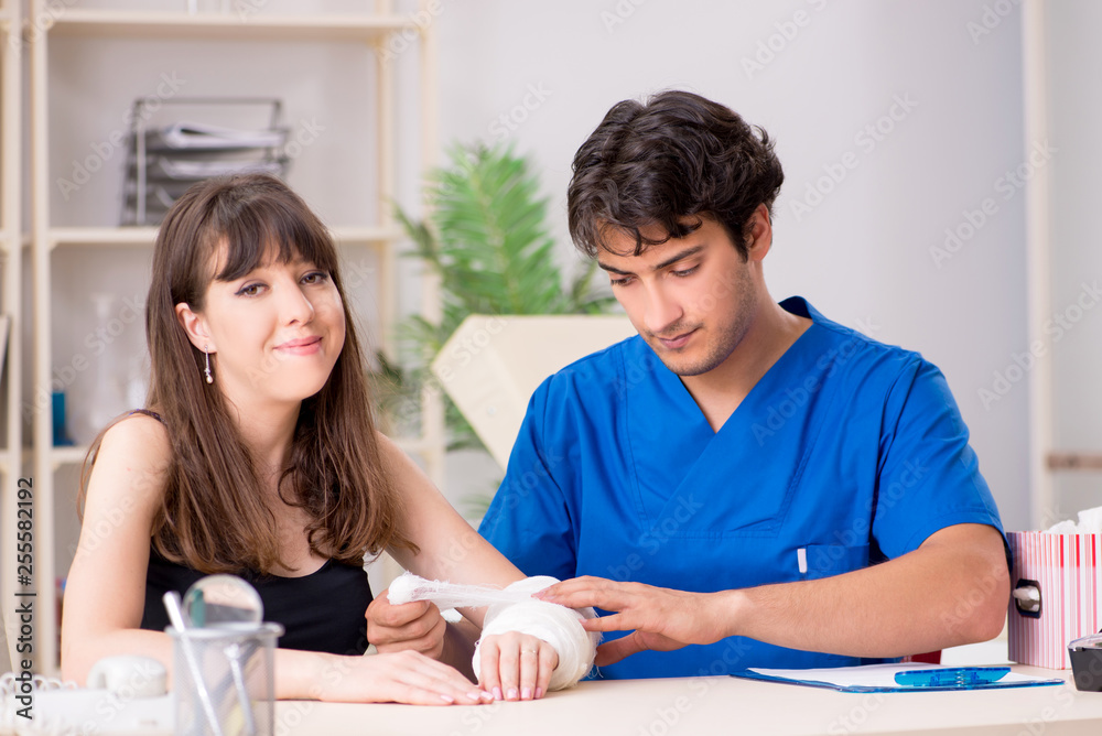 Young woman with bandaged arm visiting male doctor traumotologis Young woman with bandaged arm visiting male doctor traumotologis