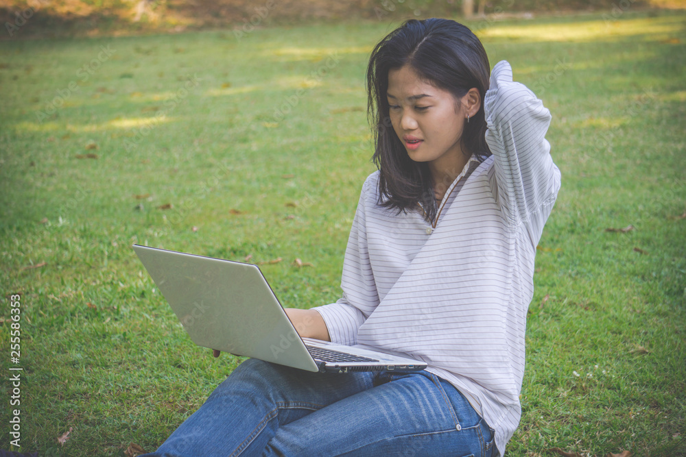 The asia woman is playing computer on a notebook.She sits and play laptop in park. The asia woman is playing computer on a notebook.She sits and play laptop in park.