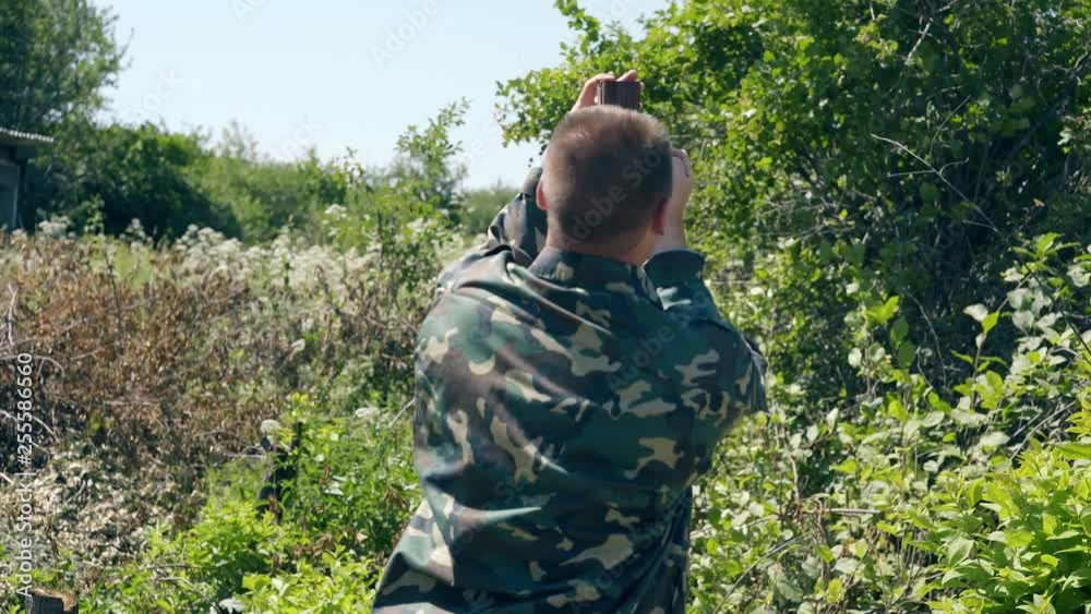 middle-aged man makes marks on metal pole top with pencil in weeds against old country house on day middle-aged man makes marks on metal pole top with pencil in weeds against old country house on day