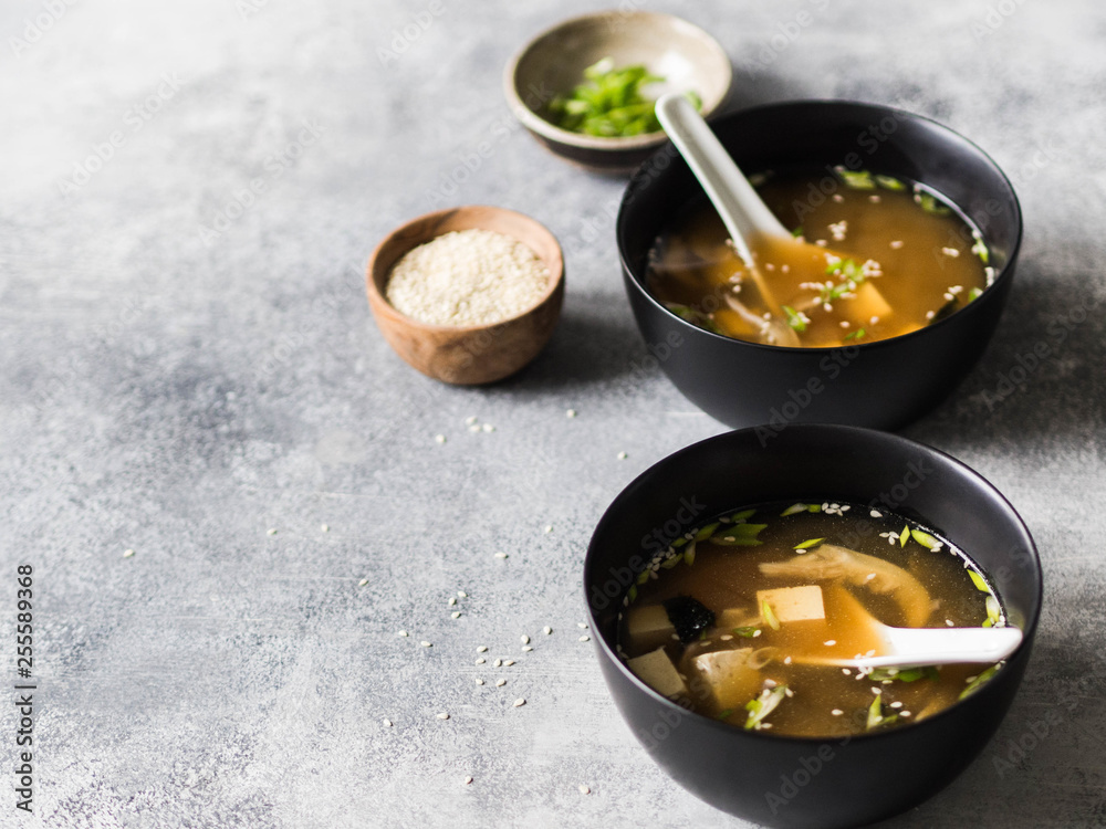 Japanese miso soup with oyster mushrooms in a black bowls with a spoon on a grey background Japanese miso soup with oyster mushrooms in a black bowls with a spoon on a grey background
