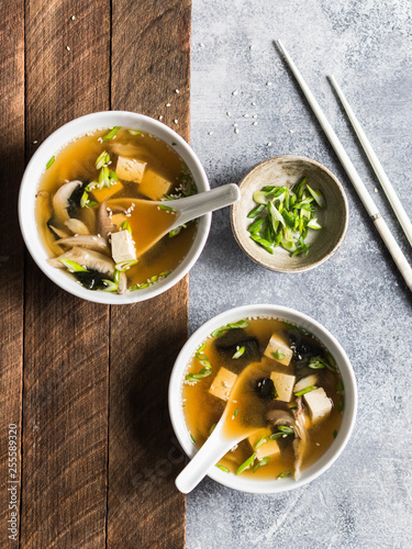 Photos Japanese miso soup with oyster mushrooms in a white bowls with a spoon and white chopsticks on a grey and wood backgrounds