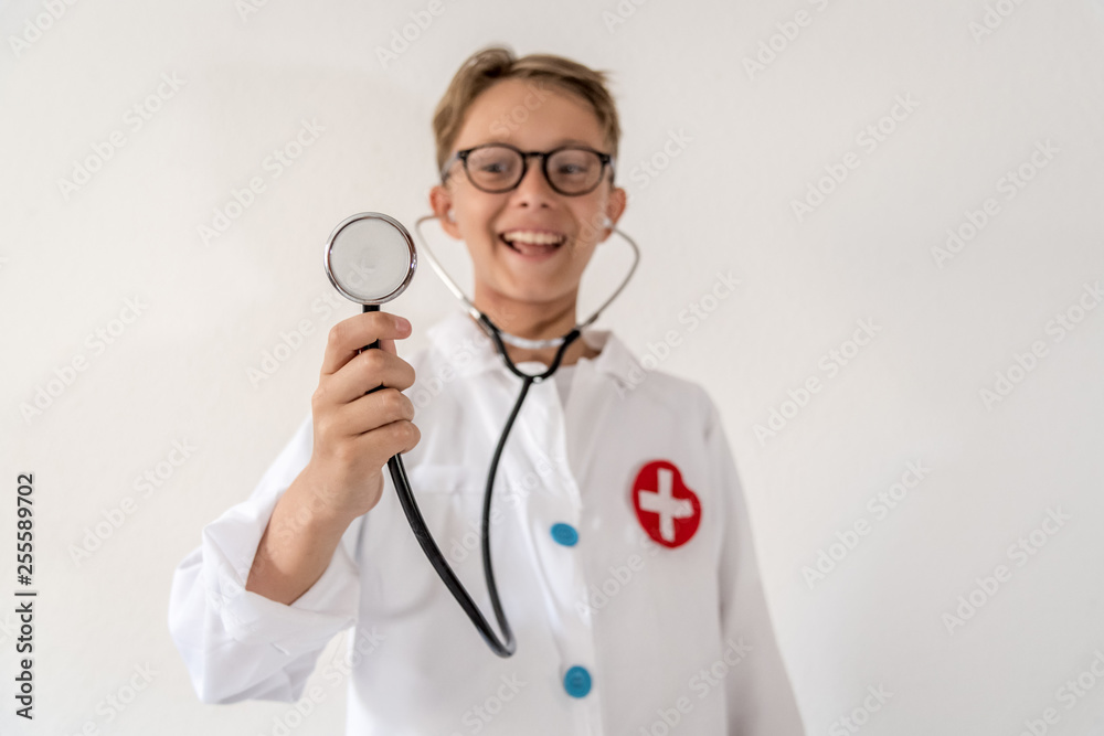 Child playing with a stethoscope and a doctor uniform ready to examine someone young boy playing with medical device and having fun dreaming about scientists Concept positive about friendly medicine Child playing with a stethoscope and a doctor uniform ready to examine someone young boy playing with medical device and having fun dreaming about scientists Concept positive about friendly medicine